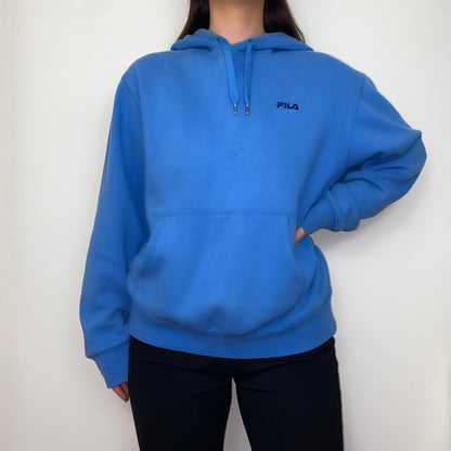 blue hoodie with black fila logo shown on a model wearing black trousers