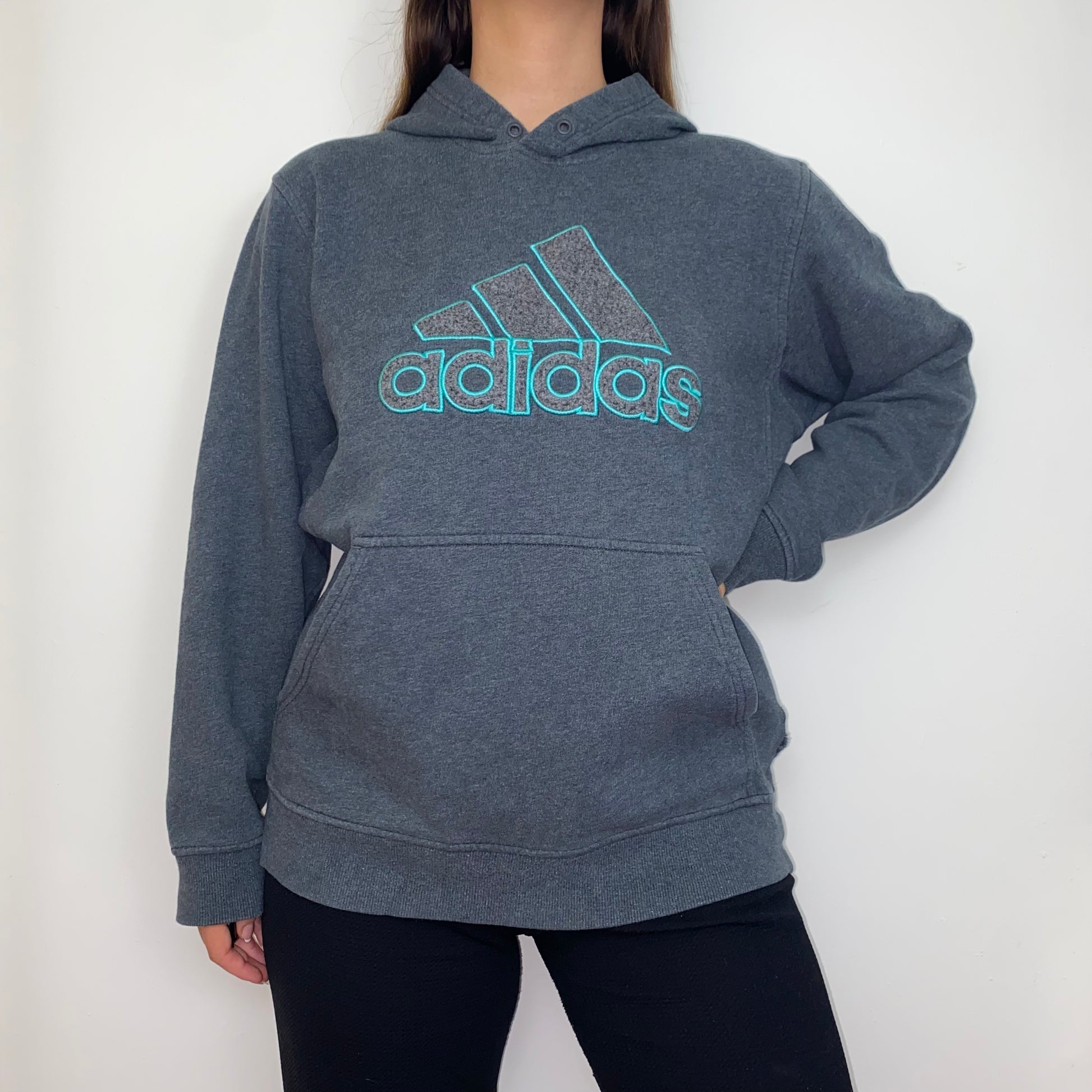 grey hoodie with blue adidas big text logo shown on a model wearing black trousers with hand on hip
