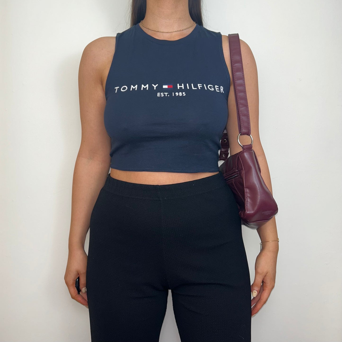 navy sleeveless crop top with white tommy hilfiger logo shown on a model wearing black trousers and a burgundy shoulder bag