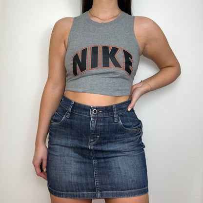 grey sleeveless crop top with orange and black nike logo shown on a model wearing a denim mini skirt