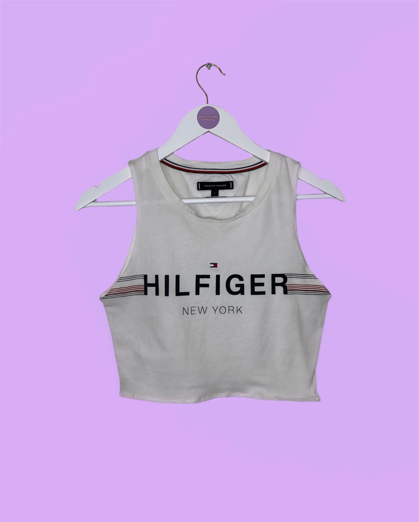 white sleeveless crop top with black hilfiger logo shown on a white clothes hanger on a lilac background