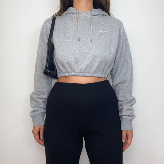 grey cropped hoodie with white nike swoosh logo shown on a model wearing black trousers and a black shoulder bag