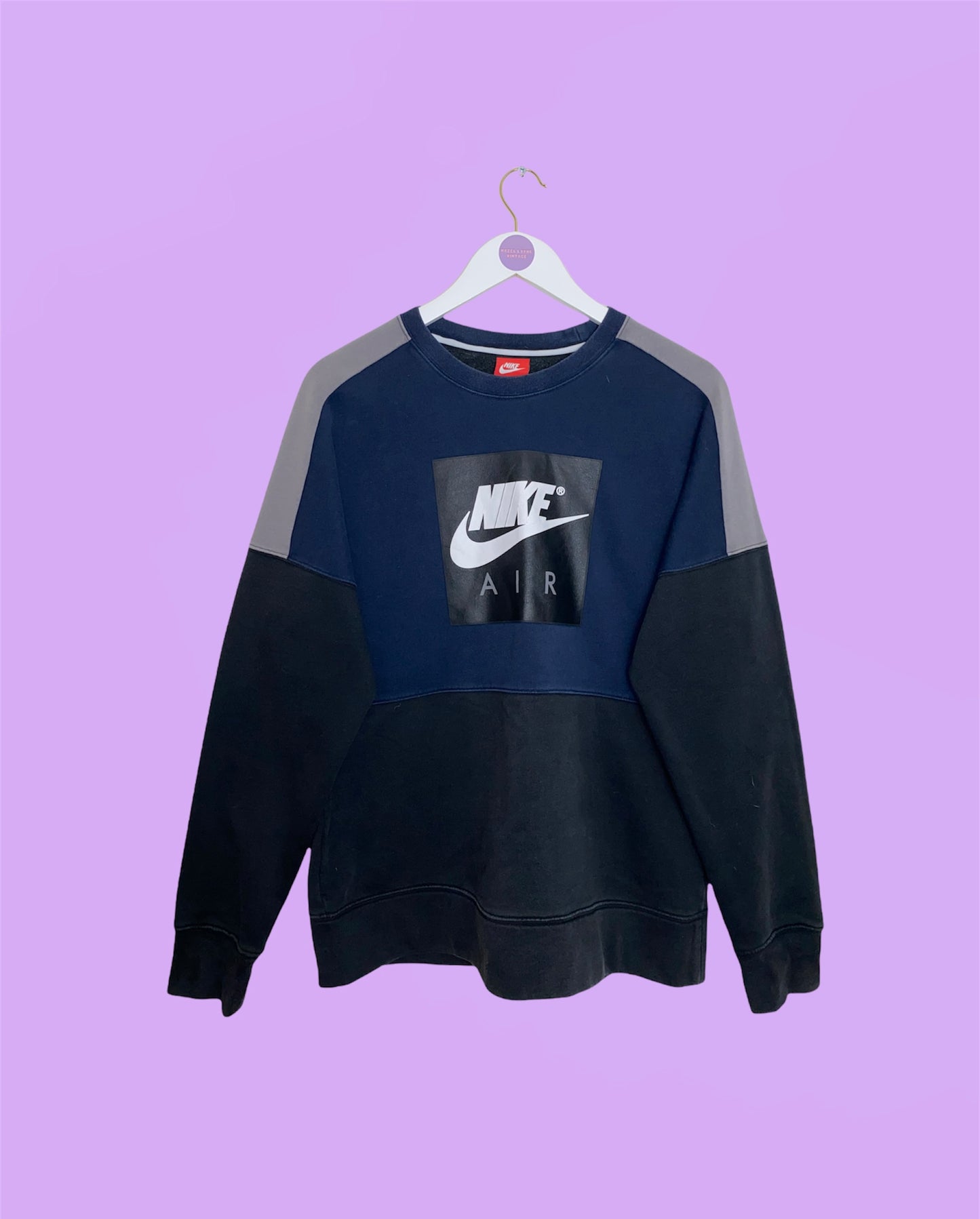 navy and black cropped sweatshirt with white nike logo shown on a white clothes hanger on a lilac background