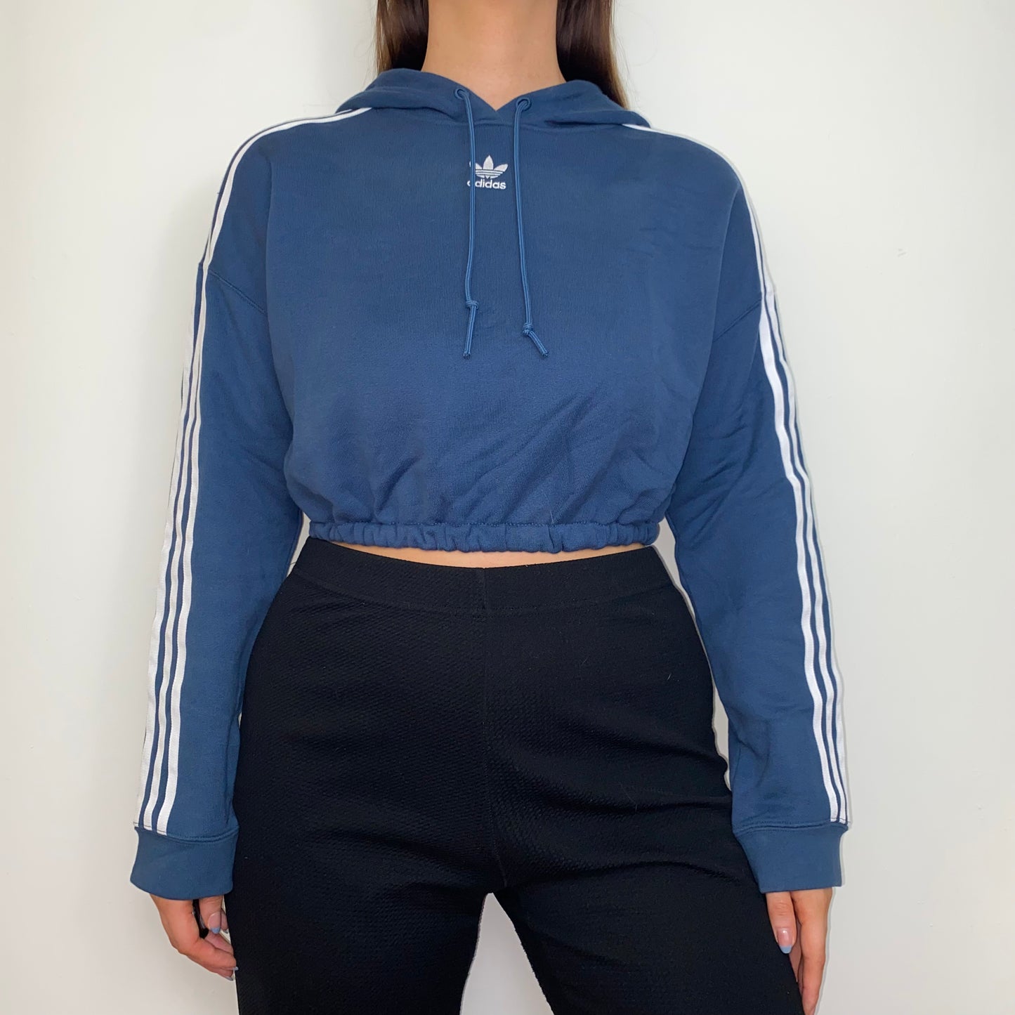 navy cropped hoodie with whtie adidas logo shown on a model wearing black trousers