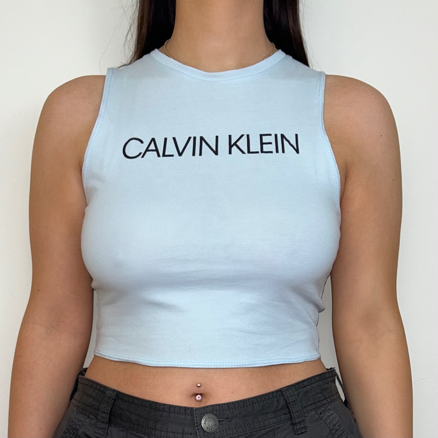 close up of baby blue sleeveless crop top with black calvin klein logo shown on a model wearing grey cargo trousers