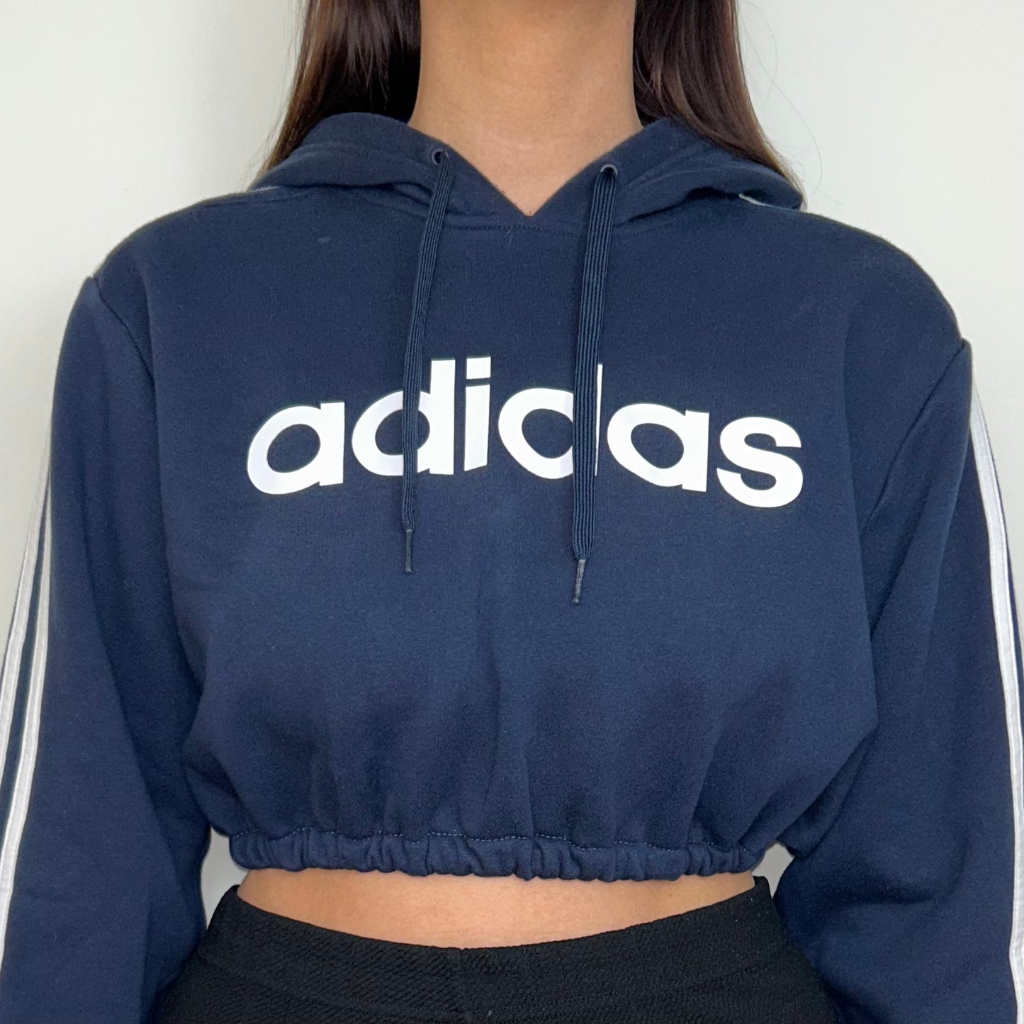 close up of navy cropped hoodie with white adidas logos shown on a model wearing black trousers