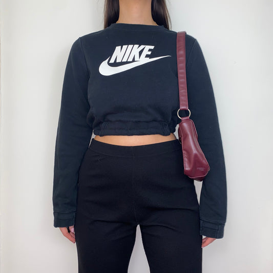 black cropped sweatshirt with white nike logo shown on a model wearing black trousers and a burgundy shoulder bag
