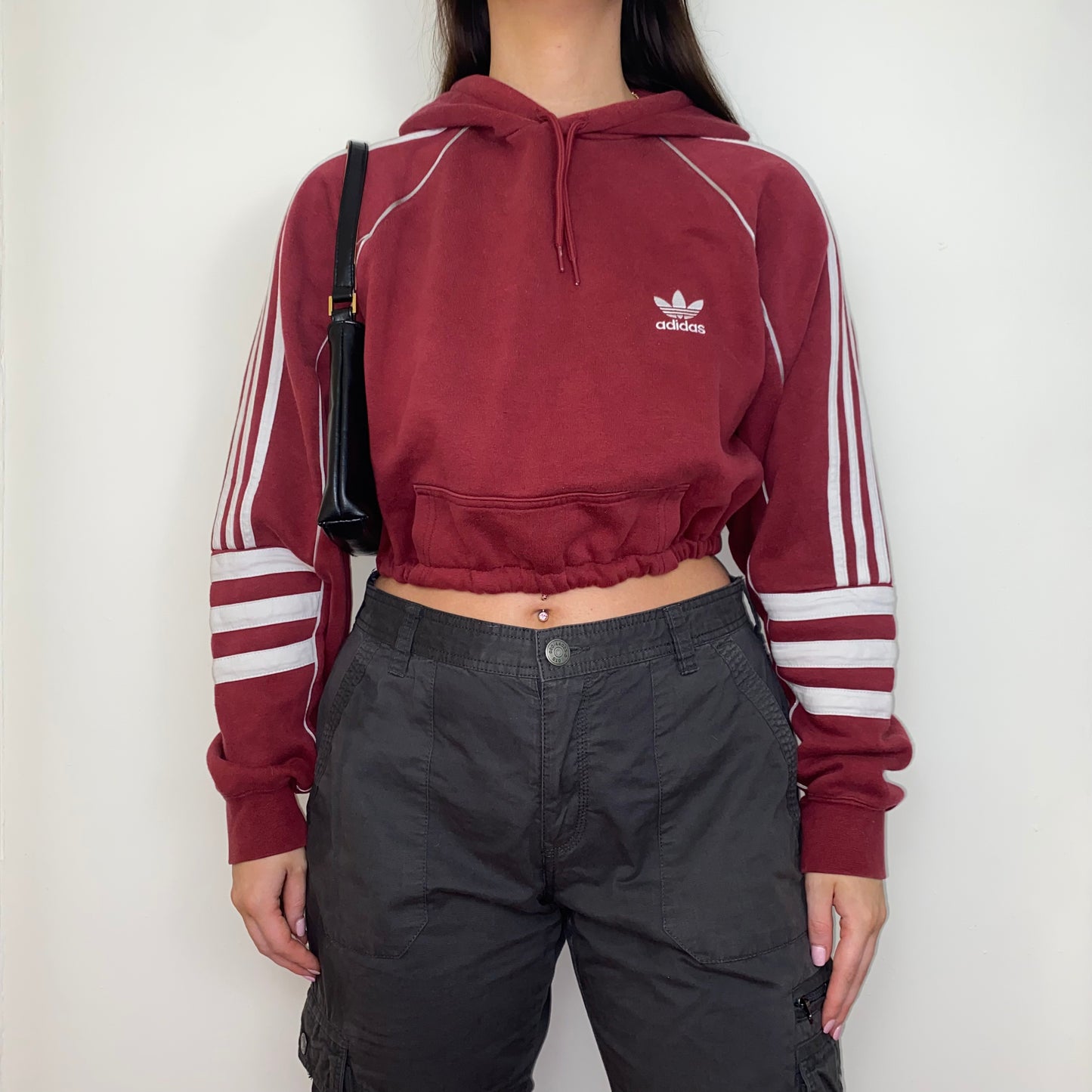 burgundy cropped hoodie with white adidas logo shown on a model wearing grey cargos and a black shoulder bag