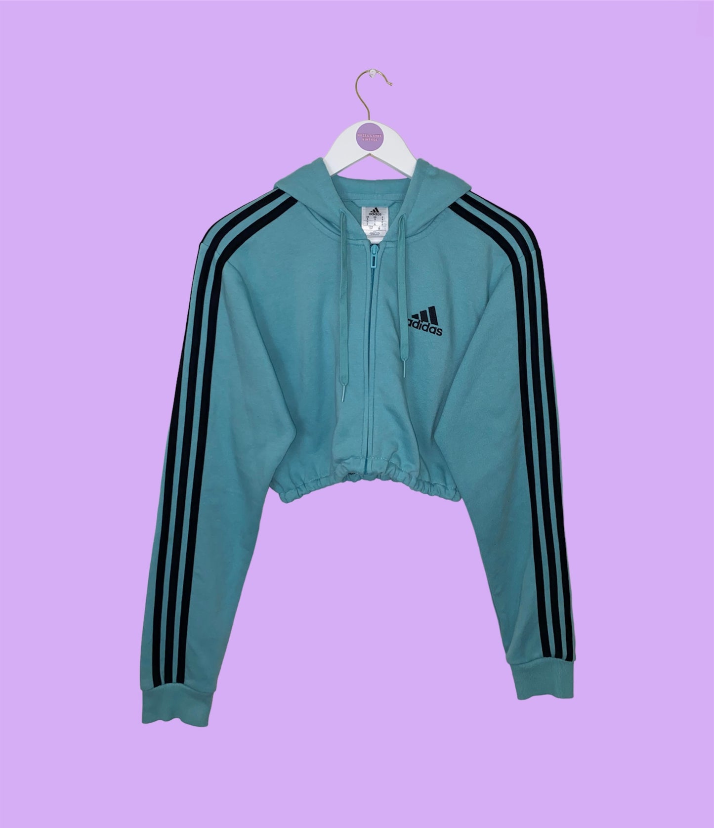 blue zip up crop hoodie with black adidas logo shown on a lilac background