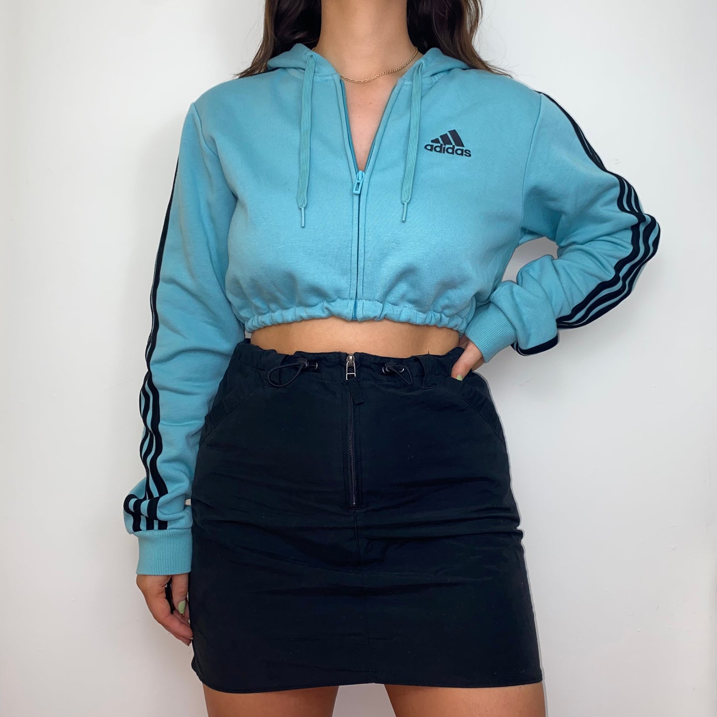 blue zip up crop hoodie with black adidas logo shown on a model wearing a black skirt