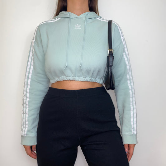 pastel green cropped hoodie with white adidas logo shown on a model wearing black trousers and a black shoulder bag