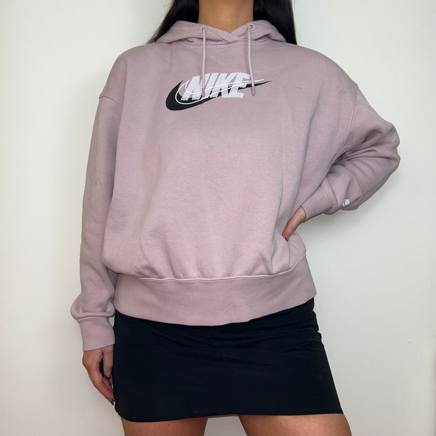 pink hoodie with white and black nike logo shown on a model wearing a black mini skirt 