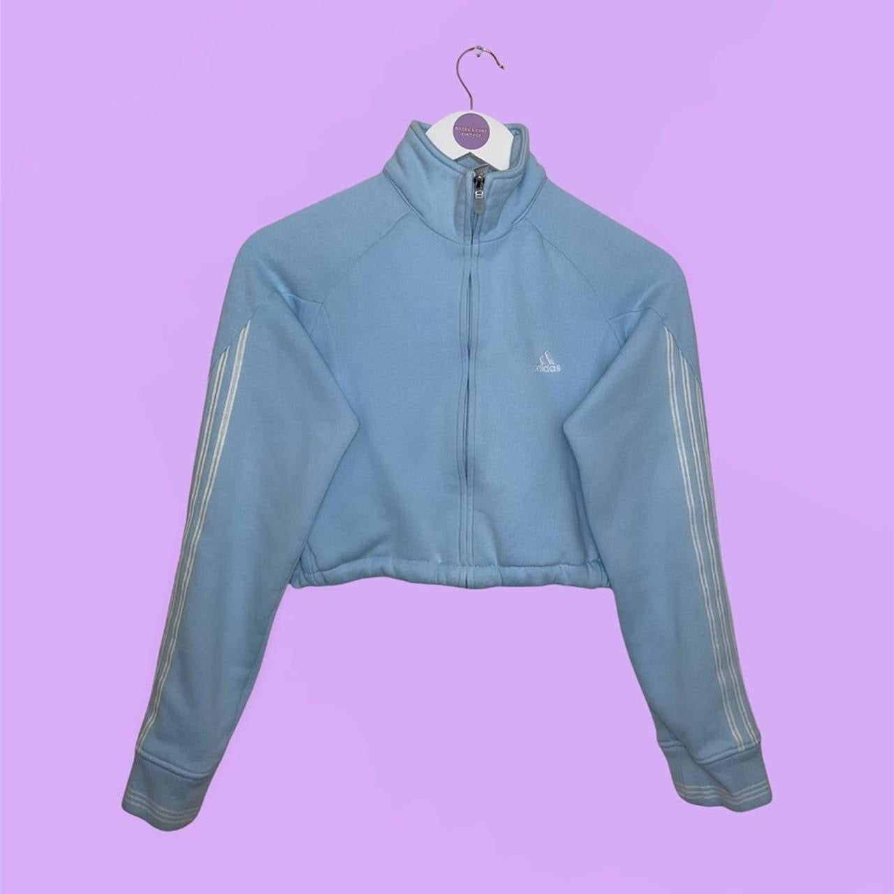 light blue zip up cropped sweatshirt with white small adidas logo on chest shown on a lilac background
