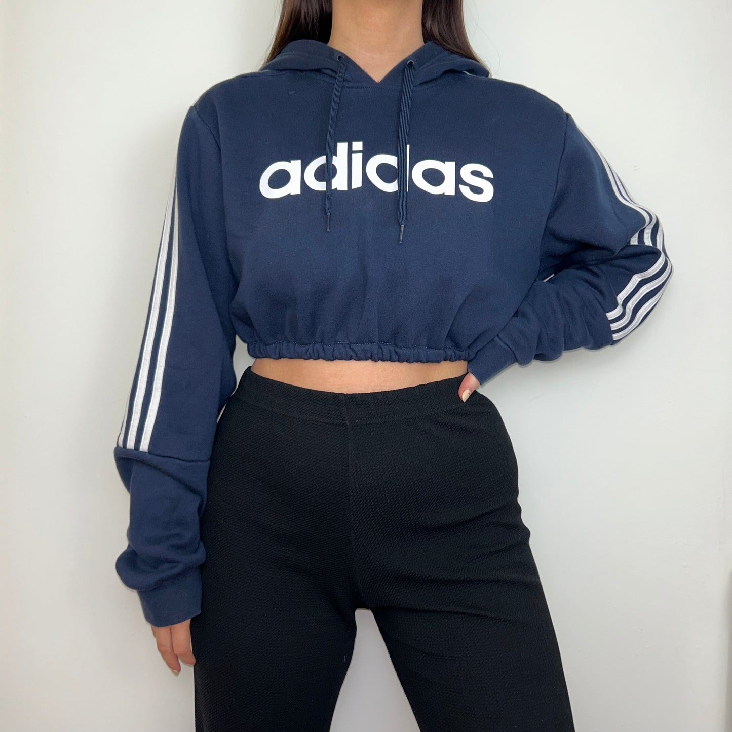 navy cropped hoodie with white adidas logos shown on a model wearing black trousers