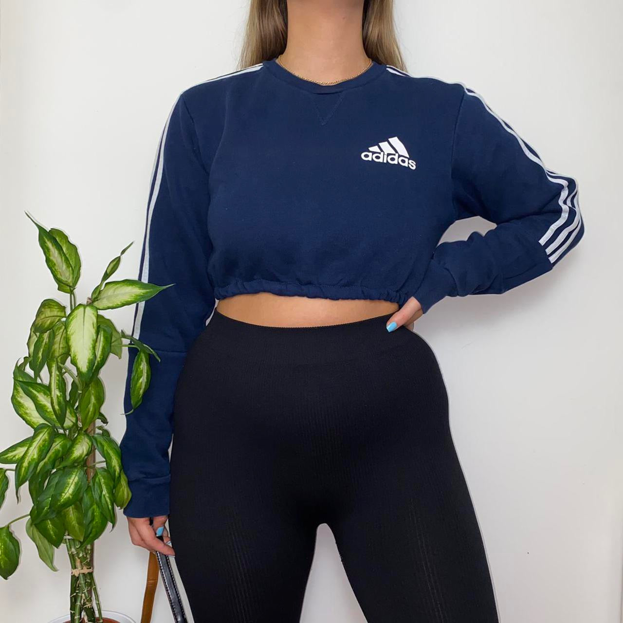 navy sweatshirt with small adidas text and symbol logo on chest with white 3 stripes on arms shown on model wearing black leggings