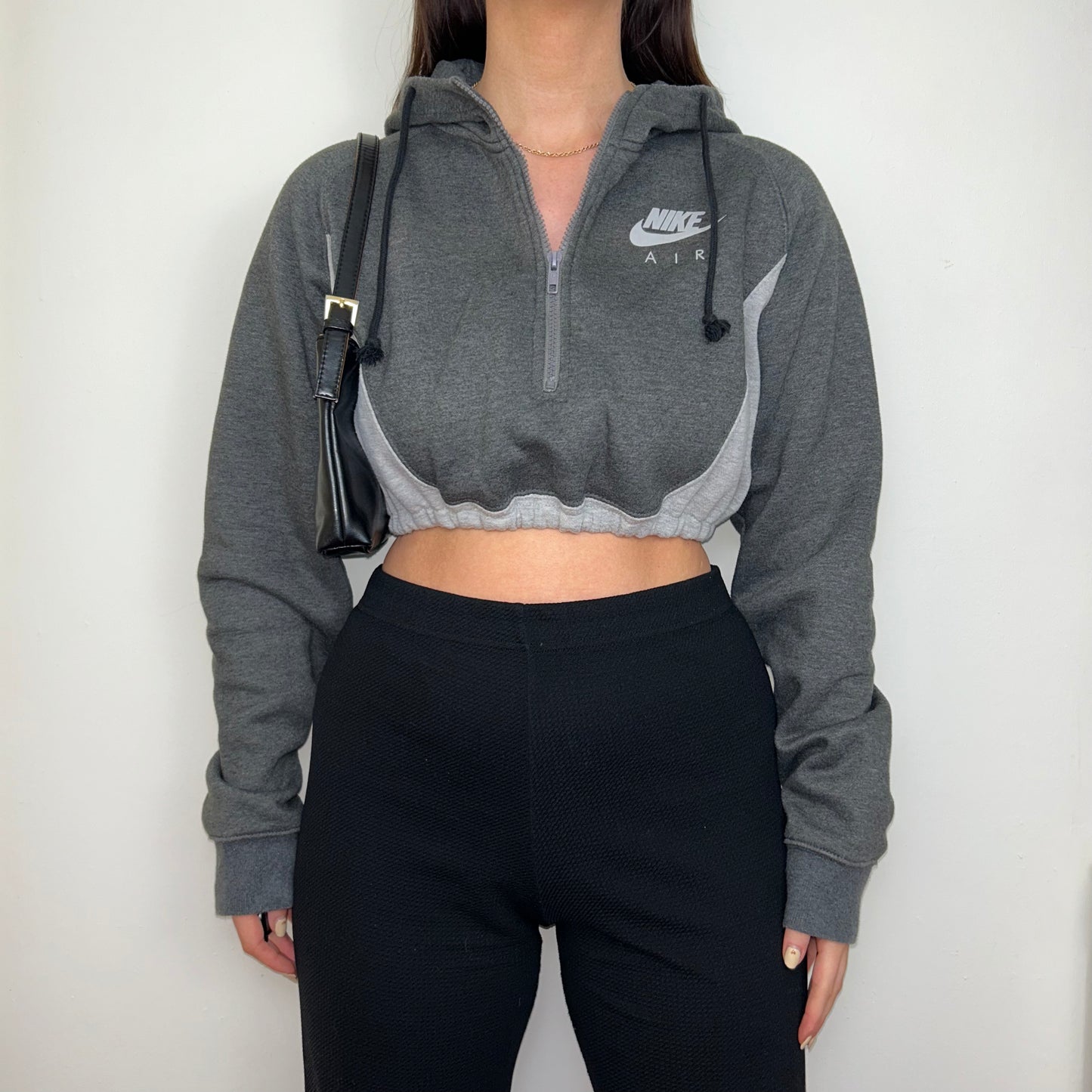 grey 1/4 zip cropped hoodie with grey nike air logo shown on a model wearing black trousers and a black shoulder bag