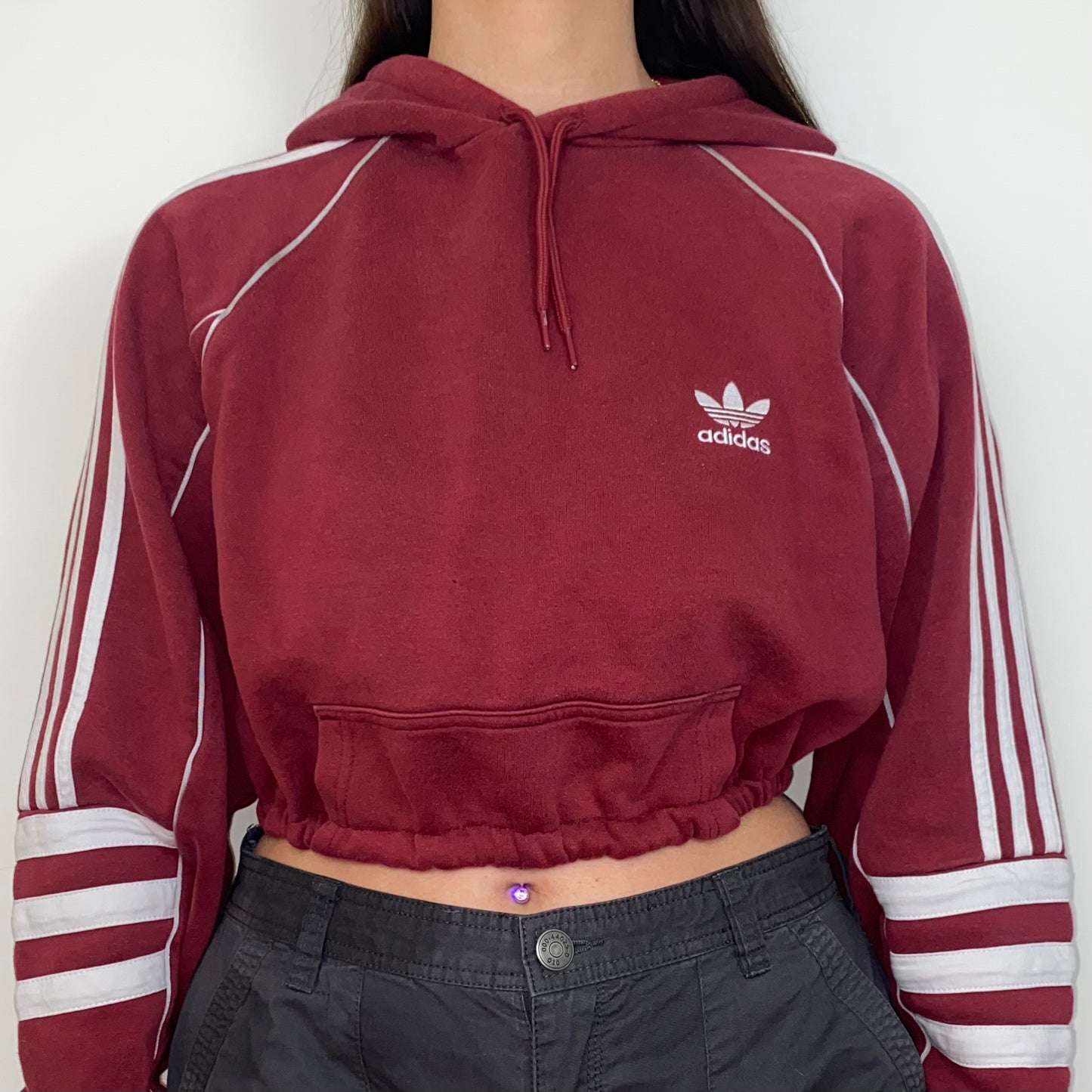 close up of burgundy cropped hoodie with white adidas logo shown on a model wearing grey cargos