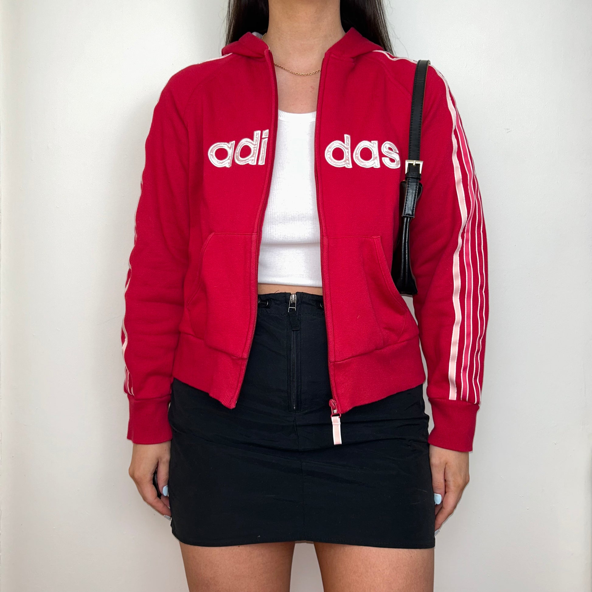 red zip up hoodie with big adidas text logo shown on a model wearing a black mini skirt with a black shoulder bag