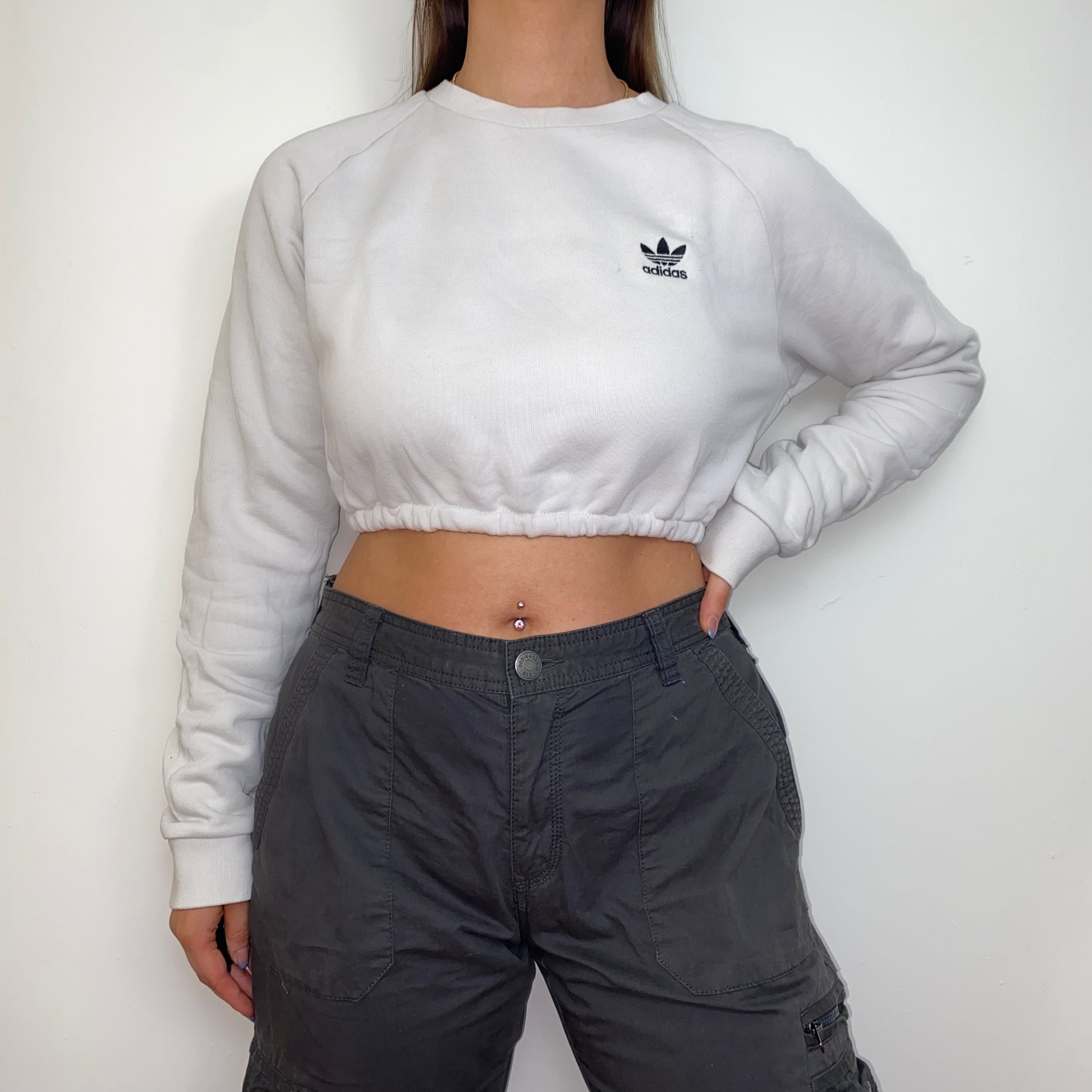 white cropped sweatshirt with black adidas logo shown on a model wearing grey cargo trousers