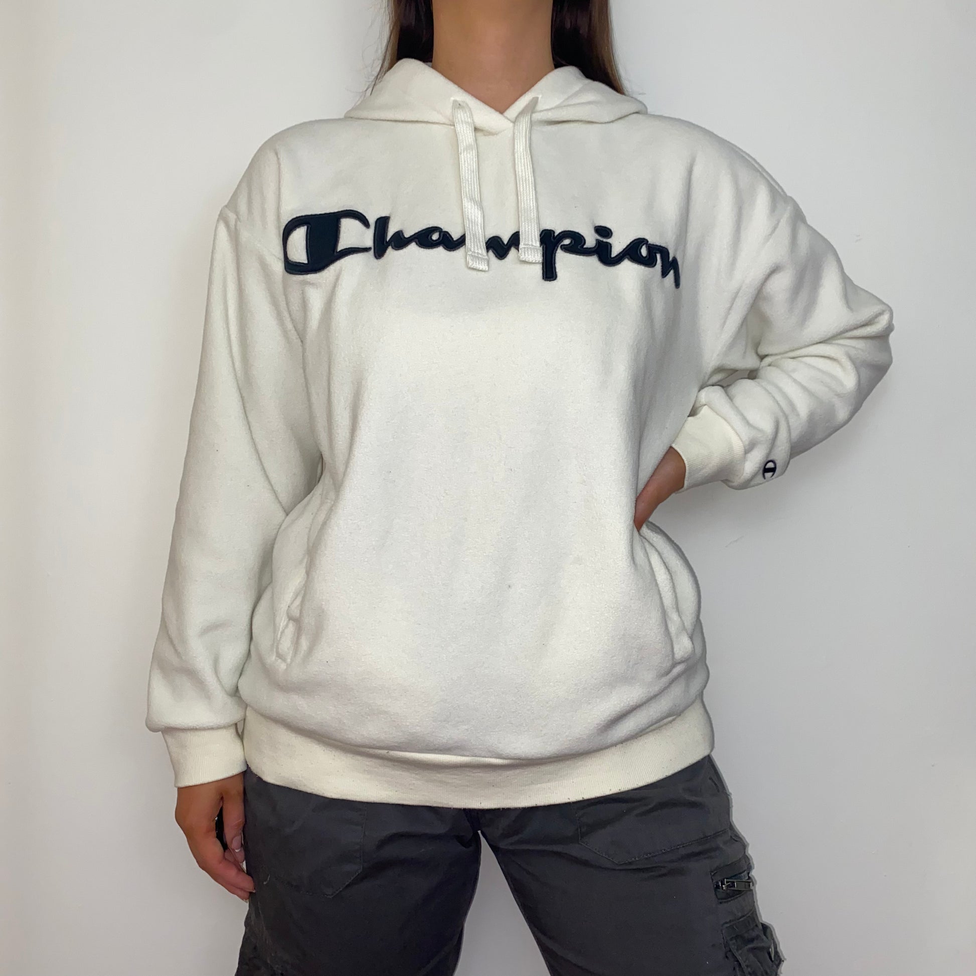 white hoodie with black big text champion logo shown on a model wearing grey cargo trousers