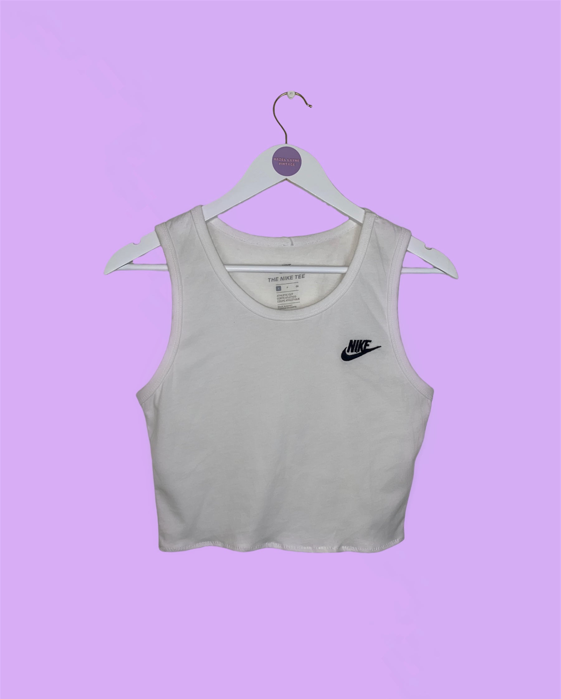 white short sleeve crop top with black nike logo shown on a white clothes hanger on a lilac background