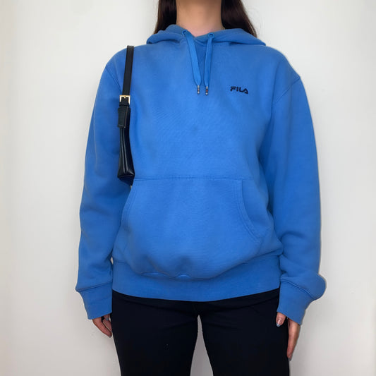 blue hoodie with black fila logo shown on a model wearing black trousers and a black shoulder bag