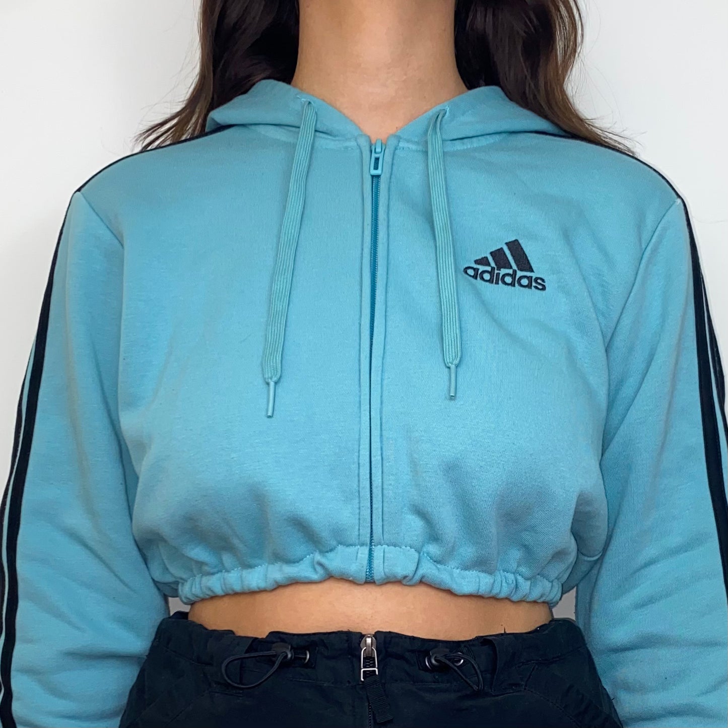 close up of a blue zip up crop hoodie with black adidas logo shown on a model