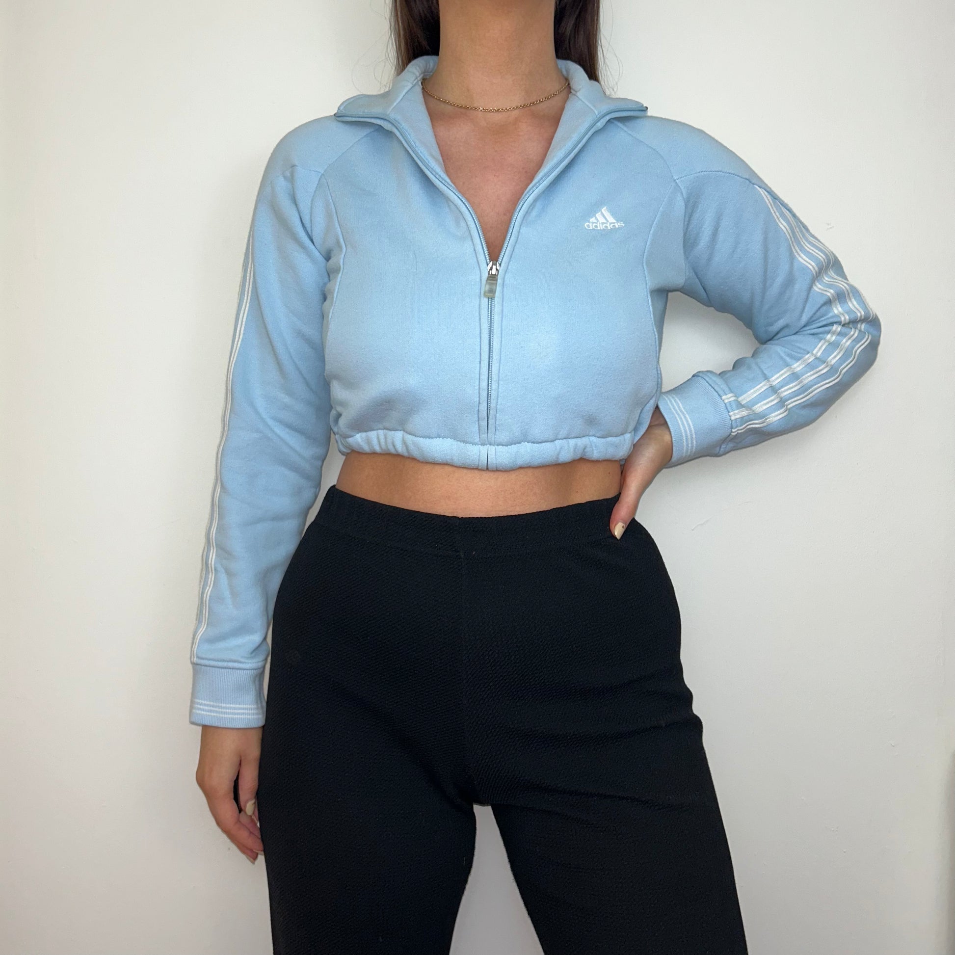 light blue 1/4 zip cropped sweatshirt with white adidas logo shown on a model wearing black trousers