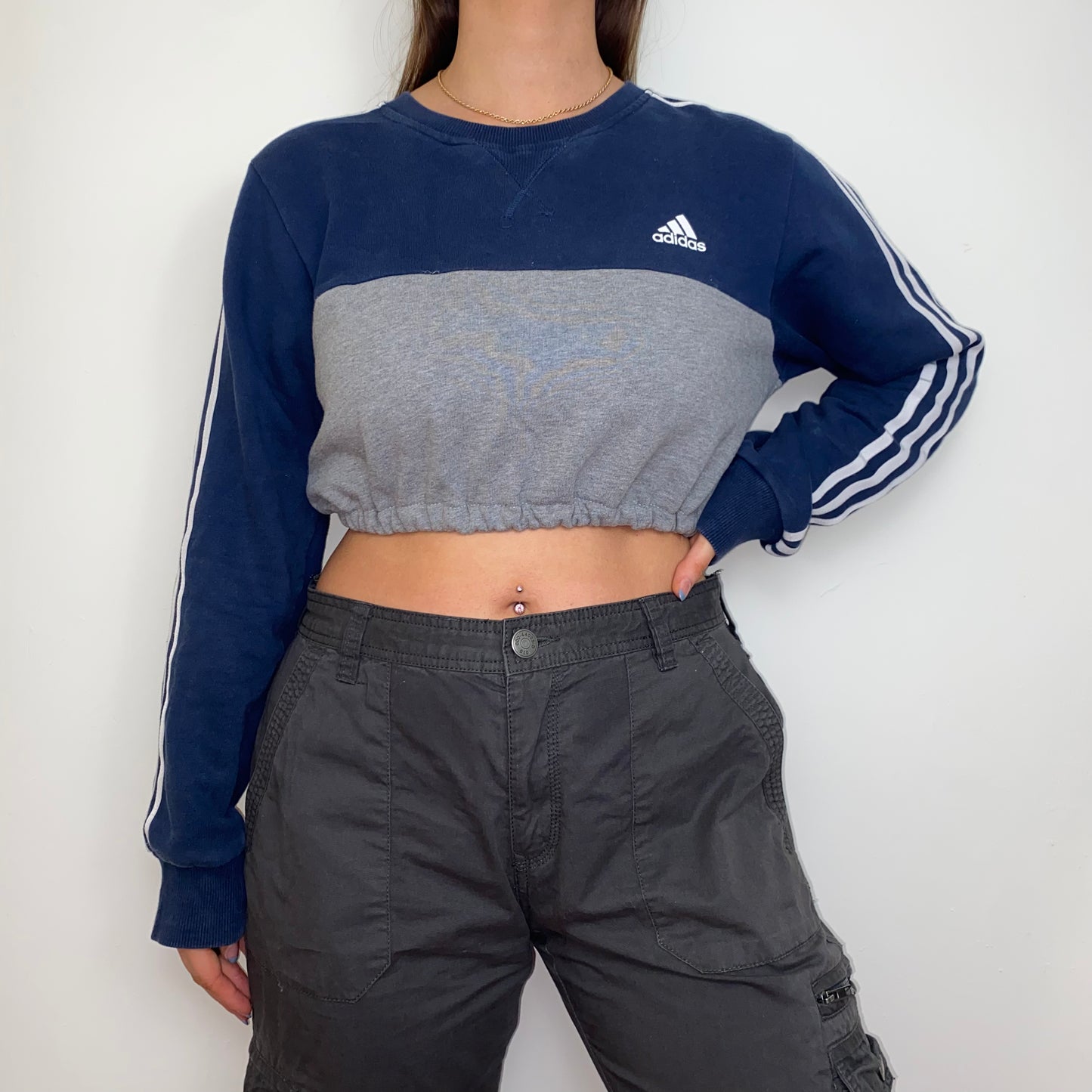 navy and grey cropped sweatshirt with white adidas logo shown on a model wearing grey cargo trousers