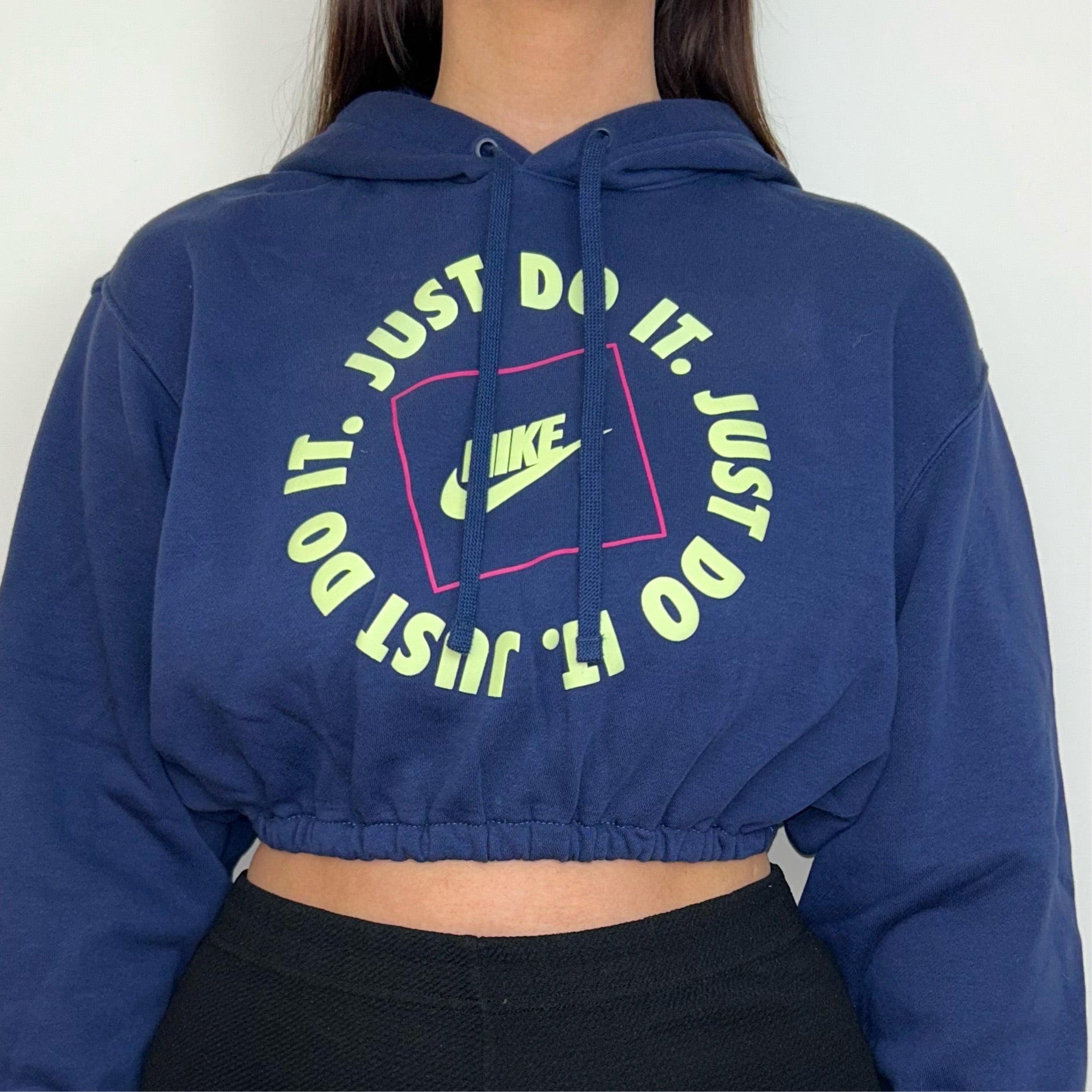 close up of navy blue cropped hoodie with yellow and pink nike text logos shown on a model wearing black trousers
