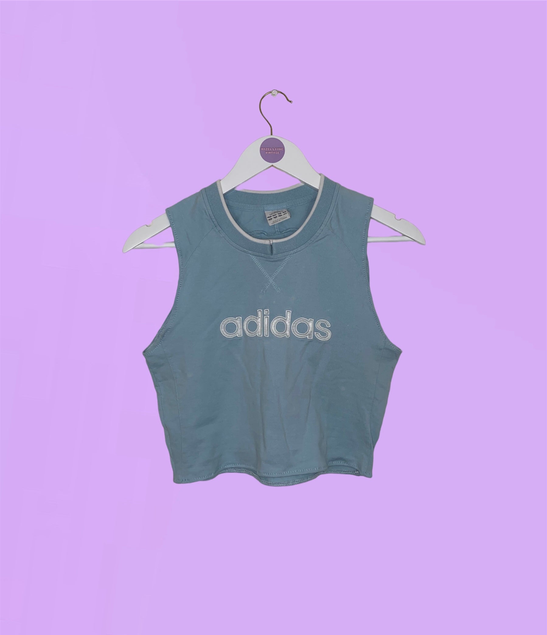 light blue sleeveless crop top with white adidas logo shown on a lilac background