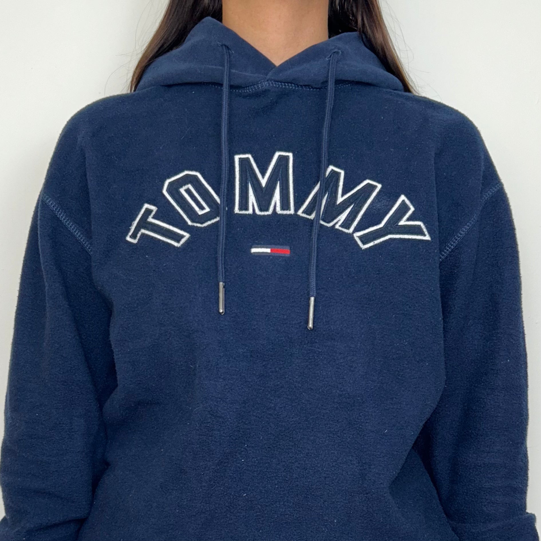 close up of navy blue fleece hoodie with white tommy logo shown on a model