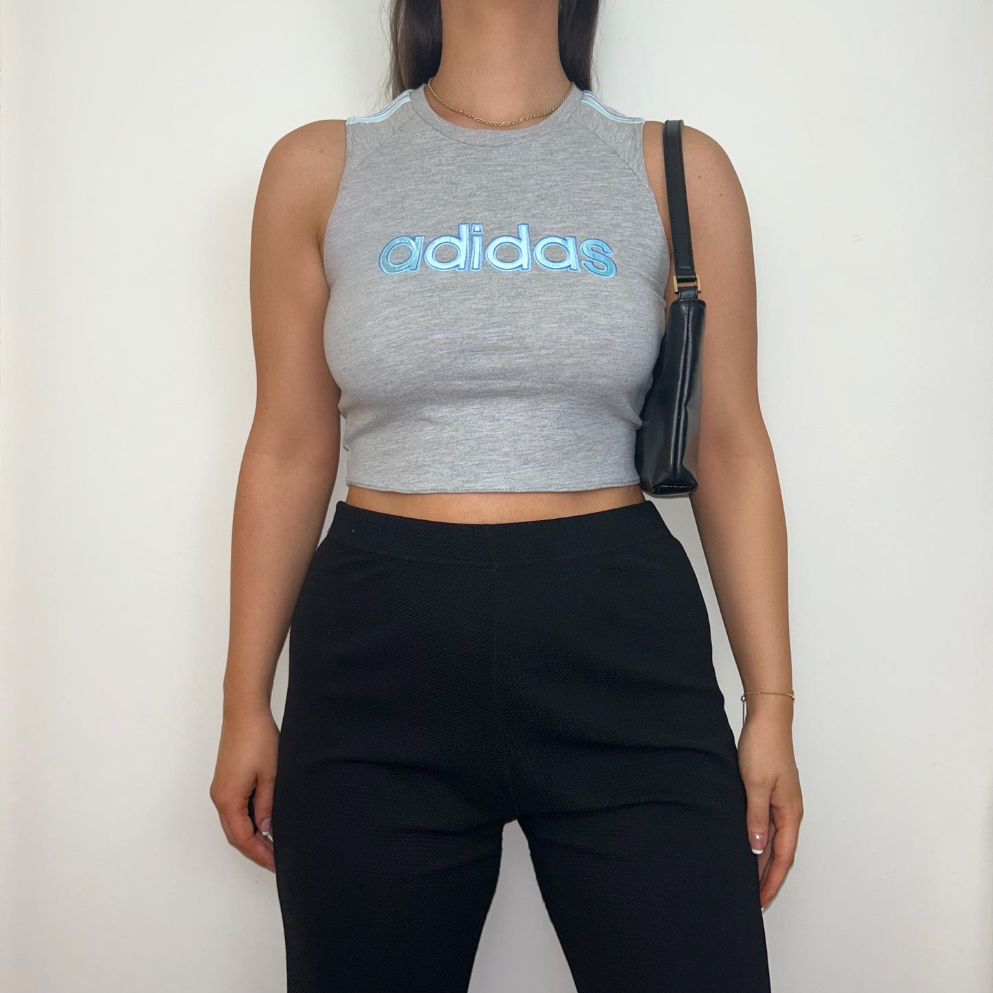 grey short sleeve crop top with light blue adidas logo shown on a model wearing black trousers and a black shoulder bag