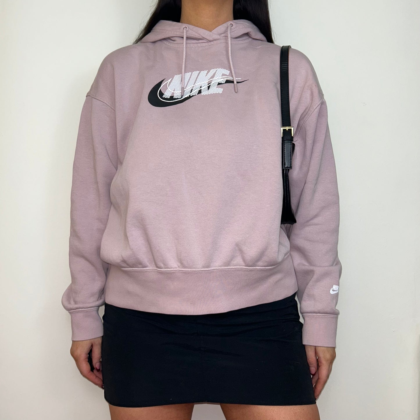 pink hoodie with white and black nike logo shown on a model wearing a black mini skirt and black shoulder bag