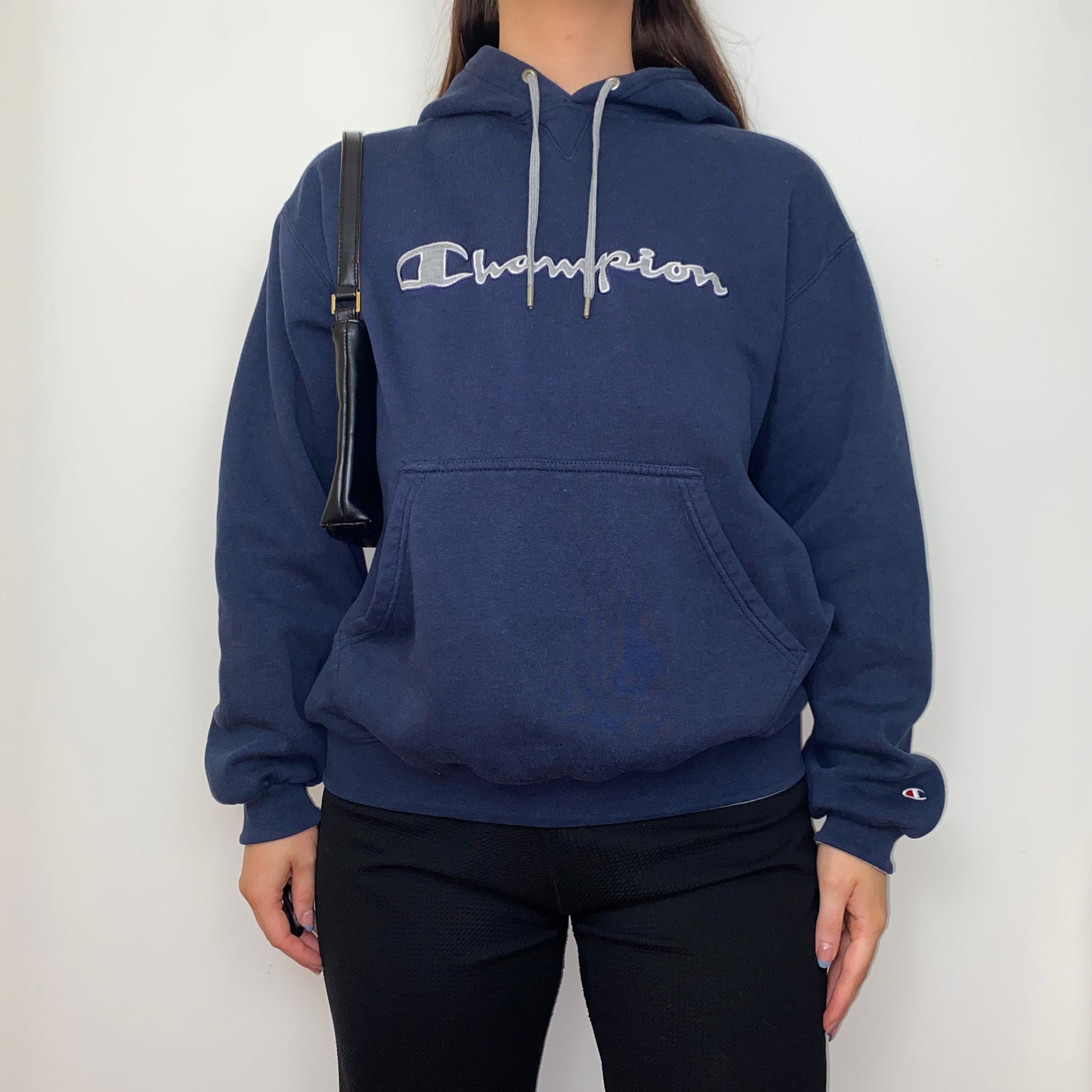 navy blue hoodie with big text champion logo shown on a model wearing black trousers and a black shoulder bag