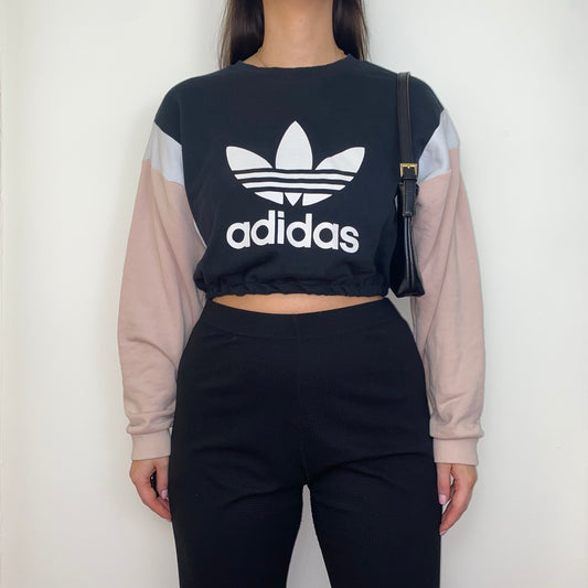 black and pink cropped sweatshirt with white adidas big text logo shown on a model wearing black trousers and a black shoulder bag