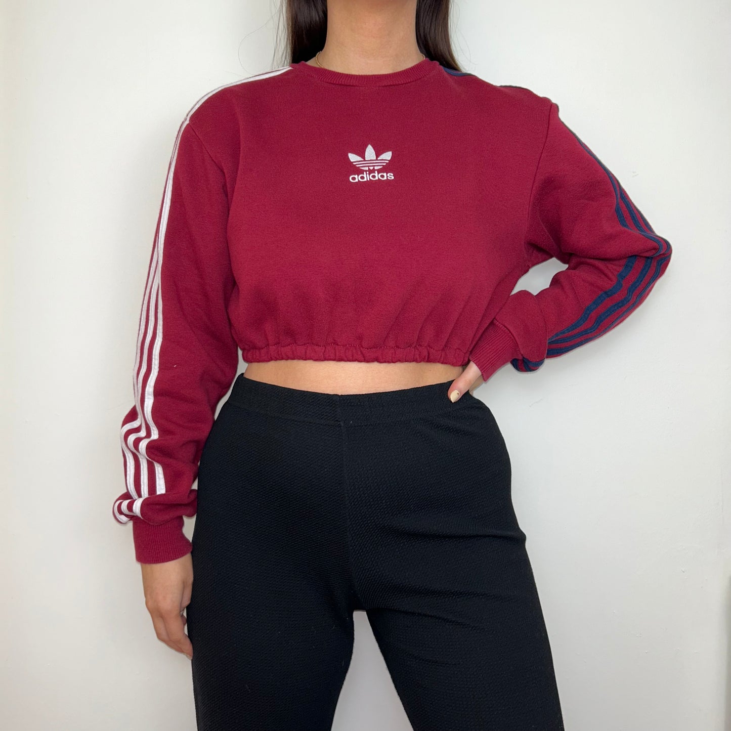 burgundy cropped sweatshirt with white adidas logo shown on a model wearing black trousers