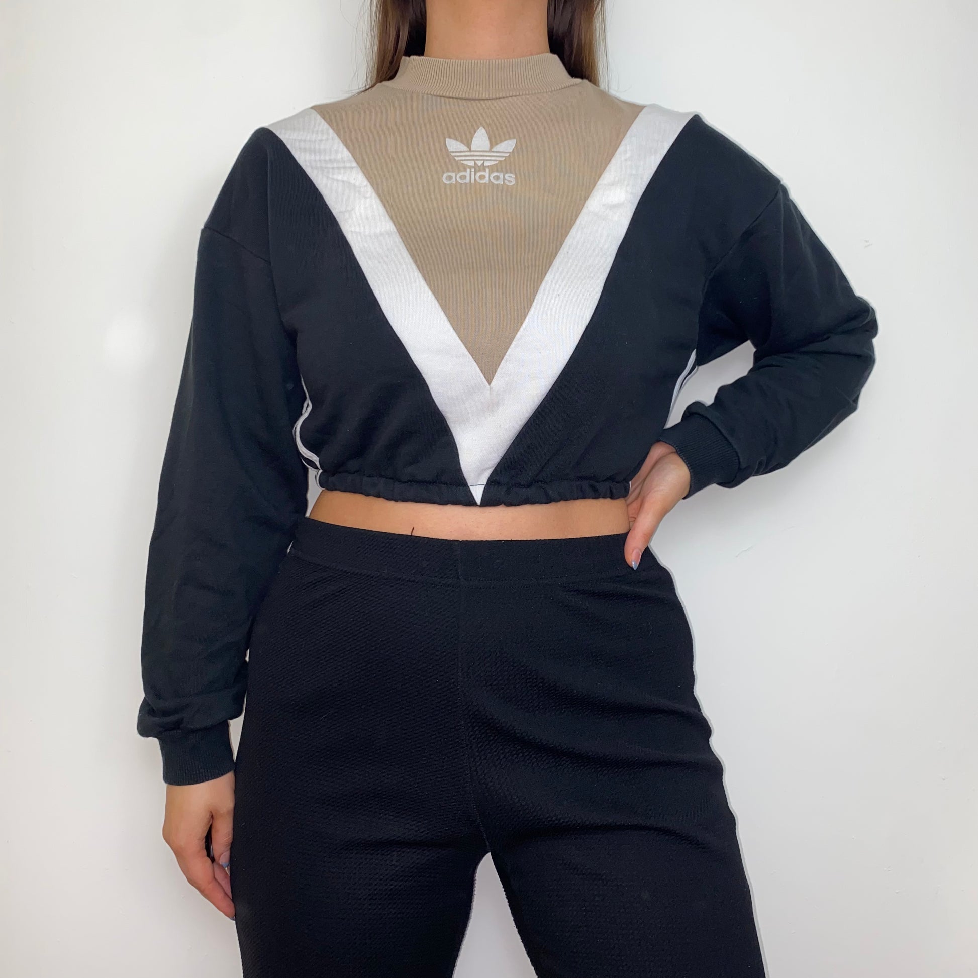black and beige cropped hoodie with white adidas logo shown on a model wearing black trousers