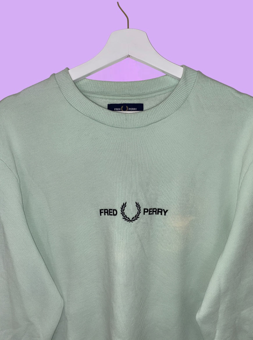 close up of green sweatshirt with black fred perry logo shown on a lilac background