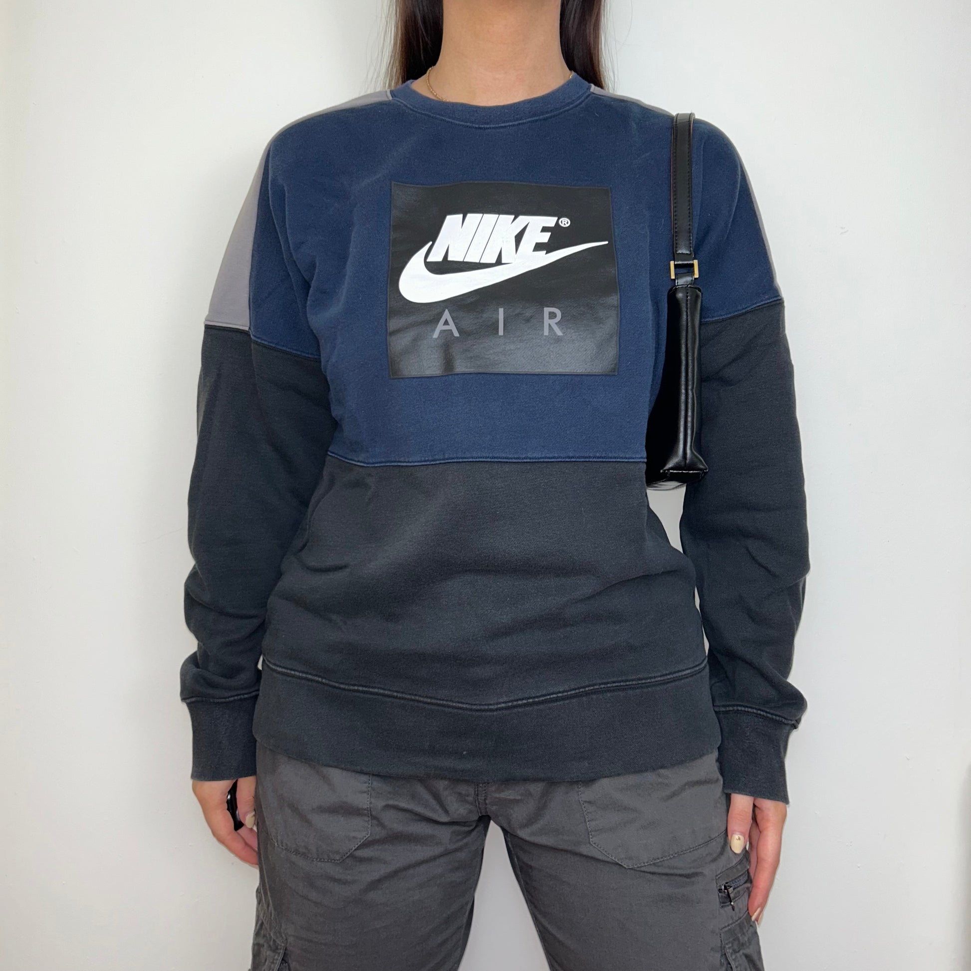 black and navy sweatshirt with white nike logo shown on a model wearing grey cargo trousers and a black shoulder bag