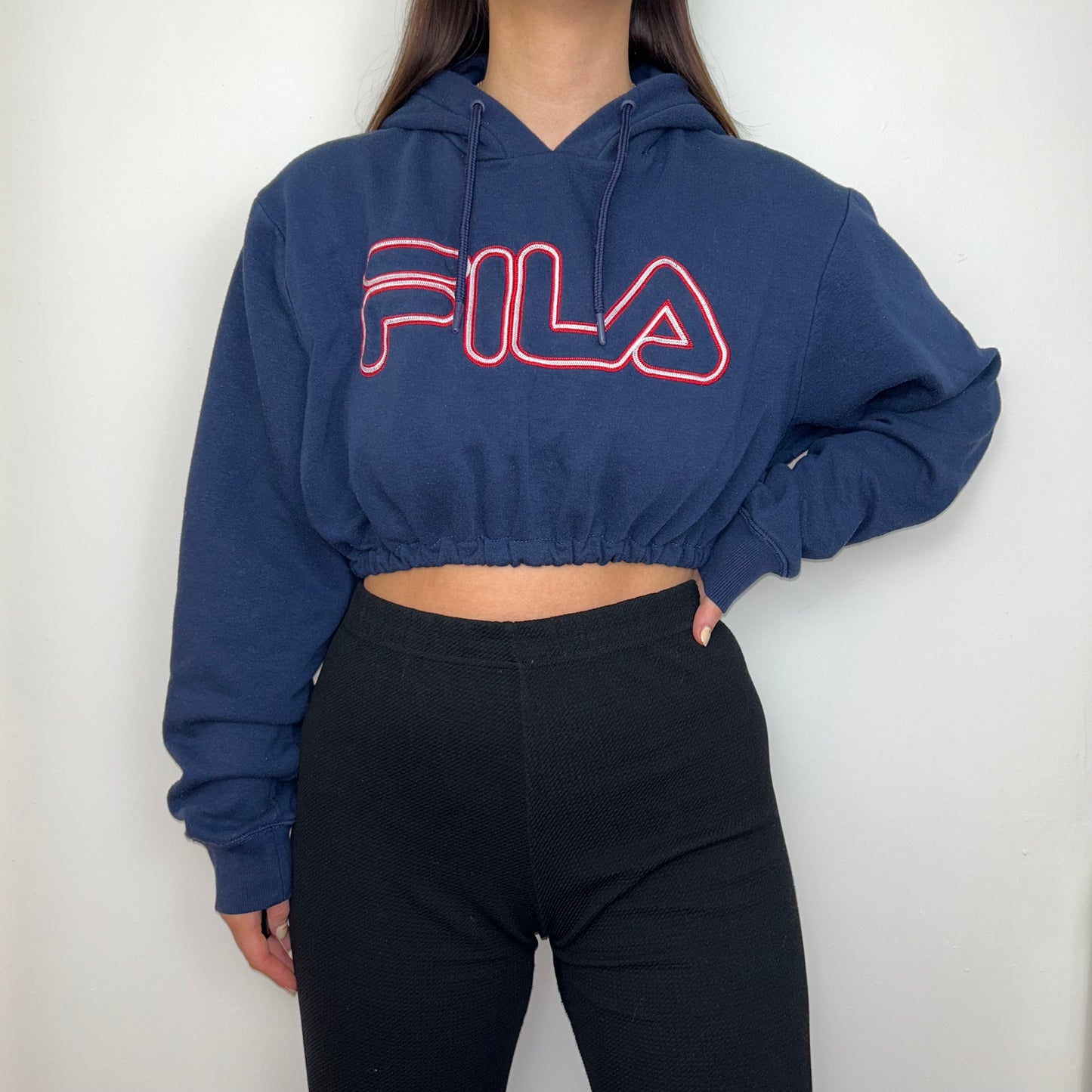 navy cropped hoodie with red big text fila logo shown on a model wearing black trousers