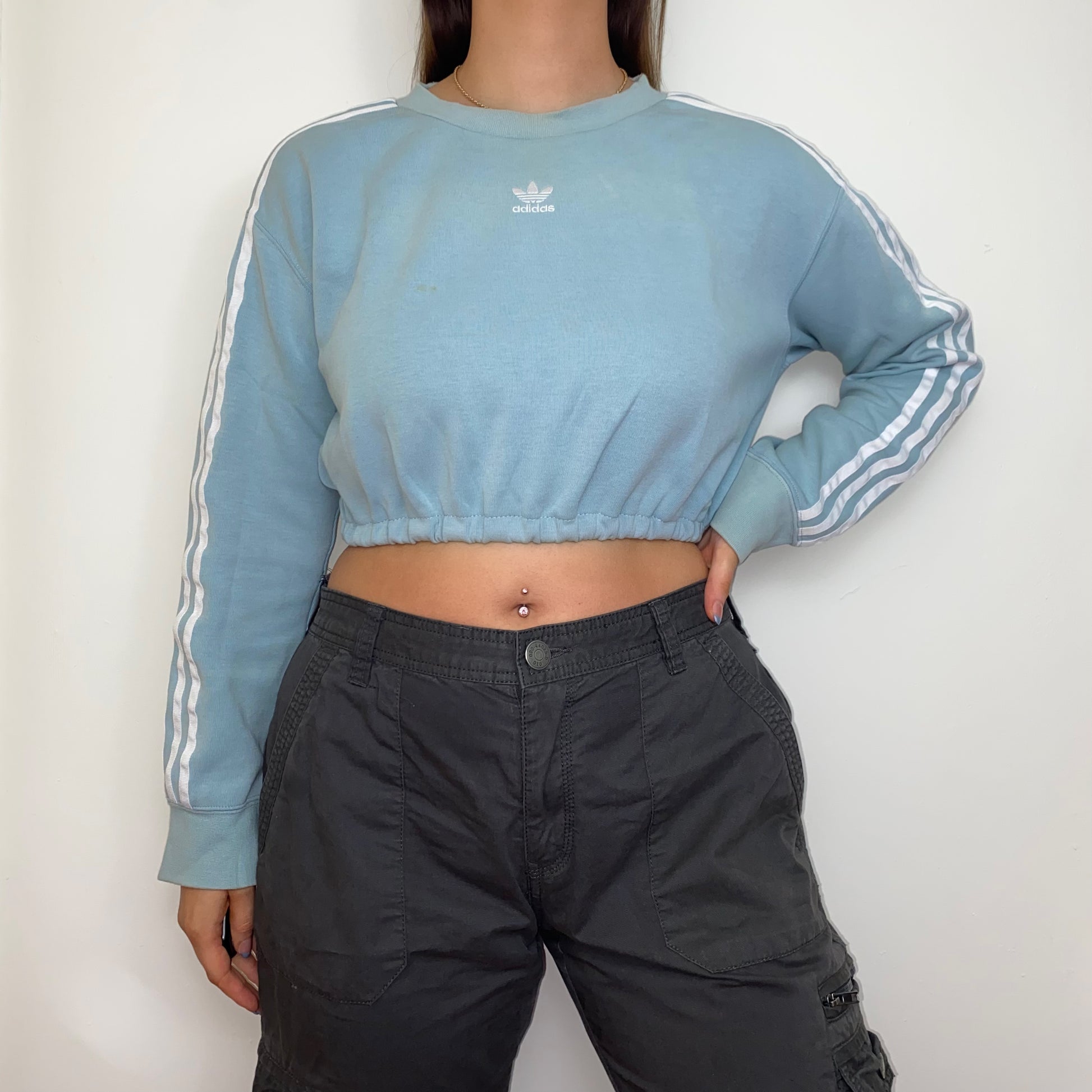 light blue cropped sweatshirt with white adidas logo shown on a model wearing grey cargo trousers