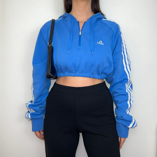 bright blue 1/4 zip cropped hoodie with white adidas logo shown on a model wearing black trousers and a black shoulder bag