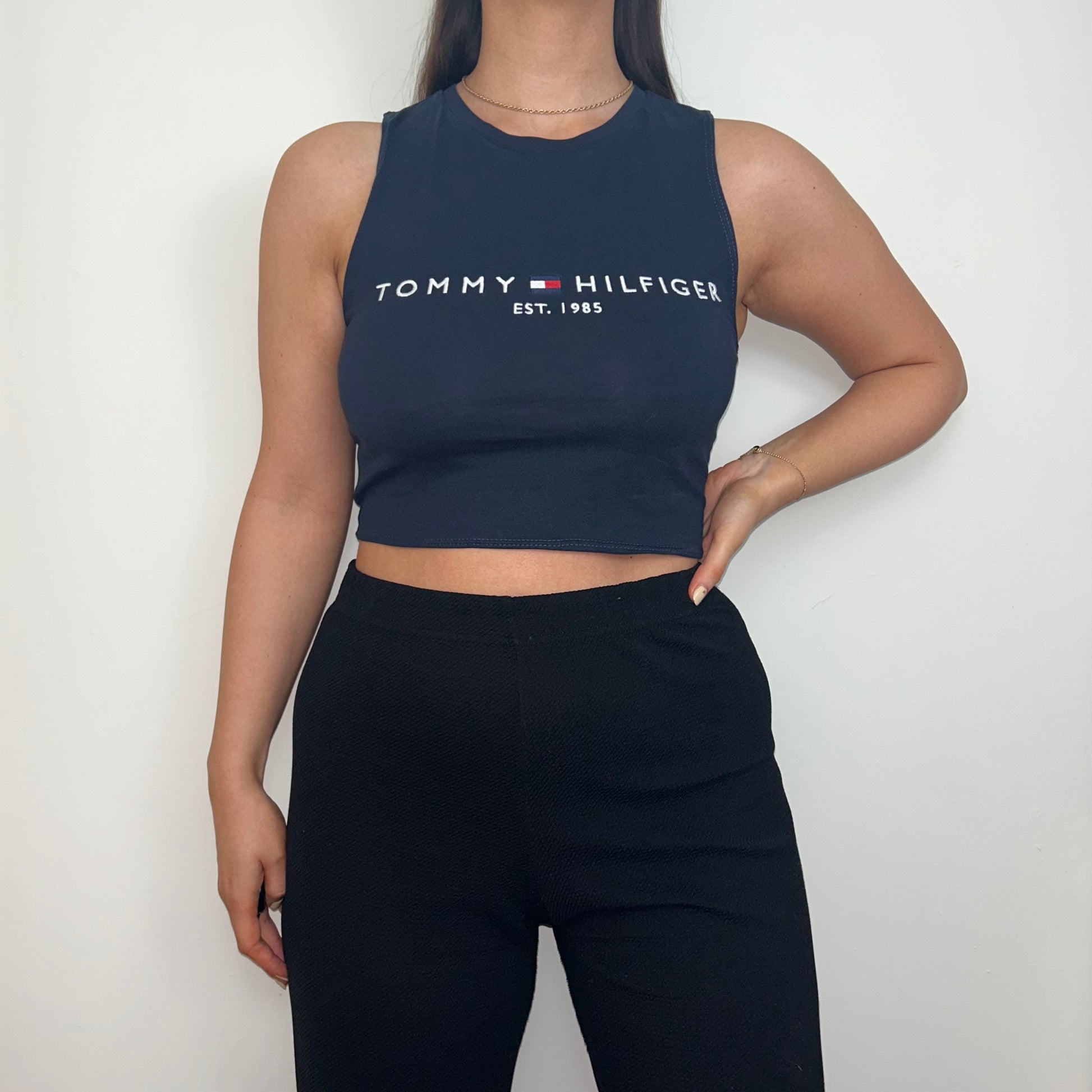 navy sleeveless crop top with white tommy hilfiger logo shown on a model wearing black trousers