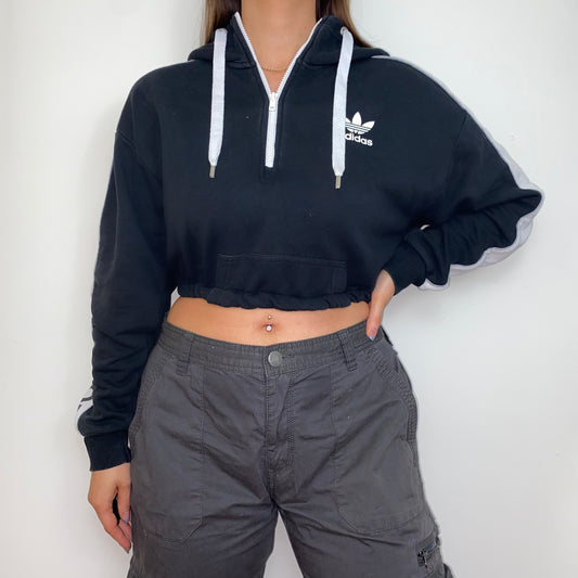 black 1/4 zip cropped hoodie with white adidas logo shown on a model wearing grey cargo trousers