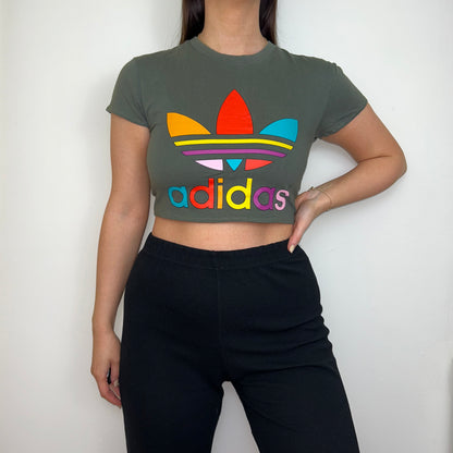 khaki short sleeve crop top with multi coloured adidas logo shown on a model wearing black trousers