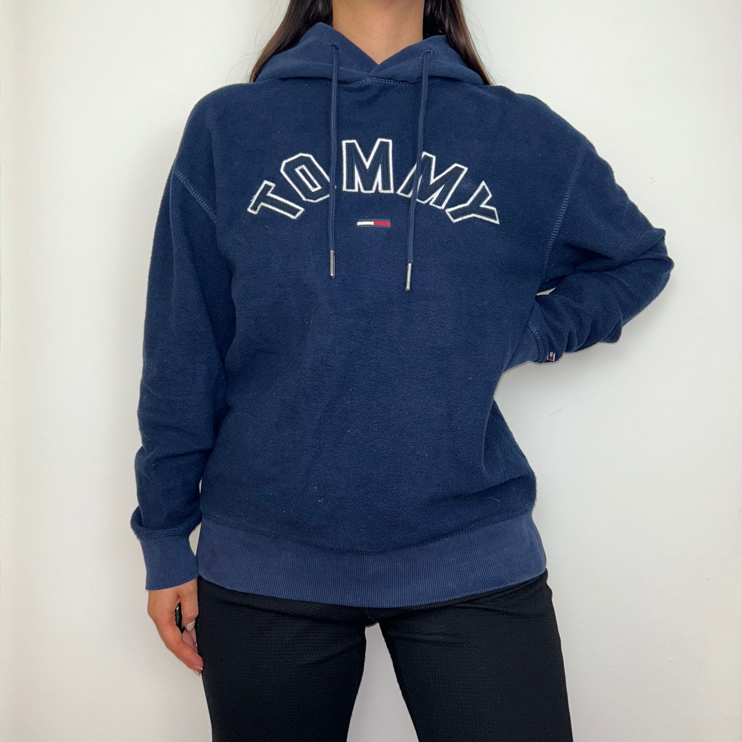 navy blue fleece hoodie with white tommy logo shown on a model wearing black trousers