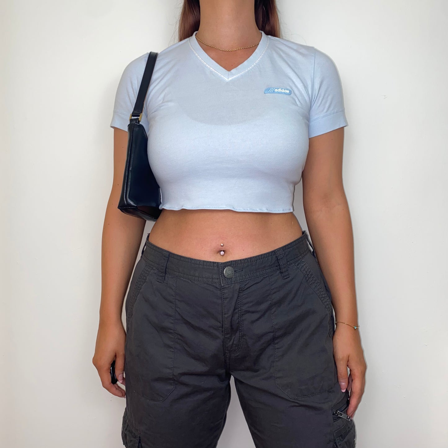 light blue short sleeve crop top with white adidas logo shown on a model wearing grey trousers and black shoulder bag