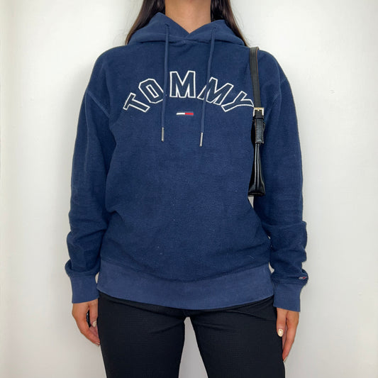 navy blue fleece hoodie with white tommy logo shown on a model wearing black trousers and a black shoulder bag