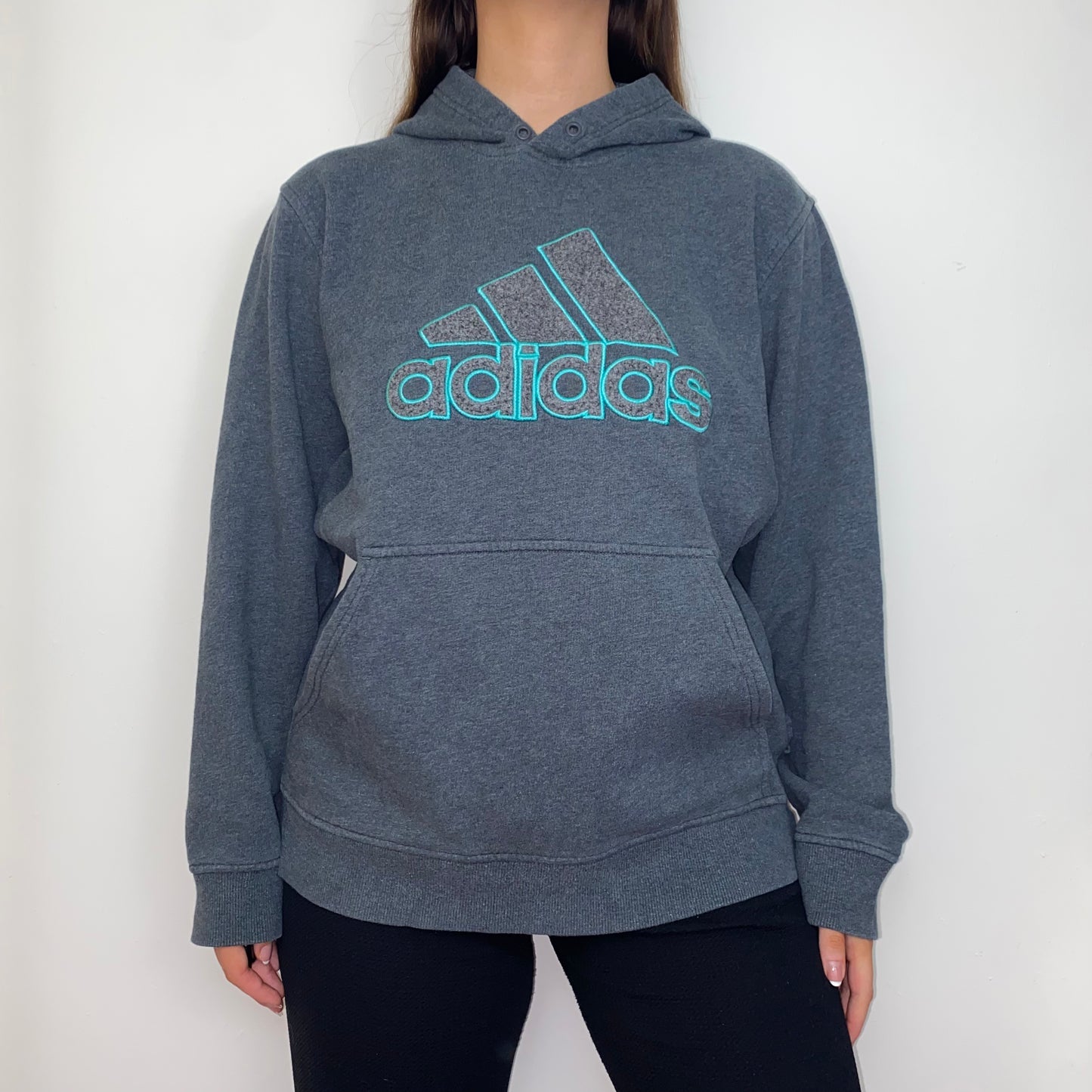 grey hoodie with blue adidas big text logo shown on a model wearing black trousers